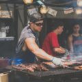 man standing infront of grill while holding tong