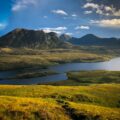 green and brown mountains near body of water under blue sky during daytime