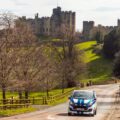 a blue and white car driving down a road in front of a castle