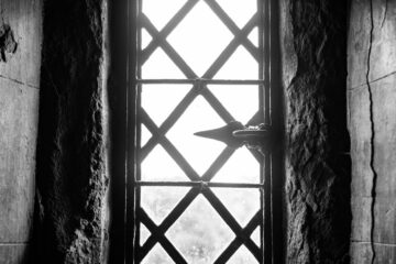 A black and white photo of a window in a stone wall