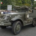 A military vehicle driving down a street past a crowd of people
