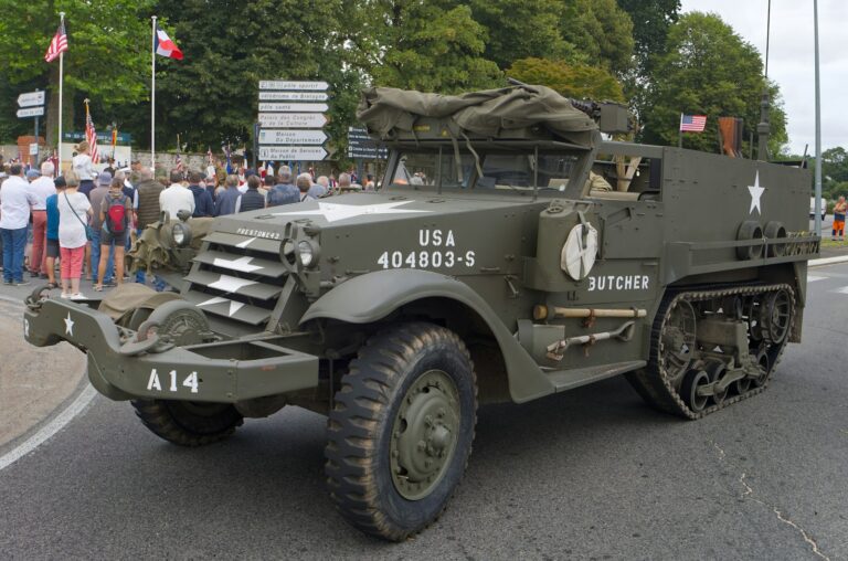 A military vehicle driving down a street past a crowd of people