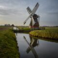 windmill near river under cloudy sky during daytime