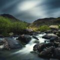 time lapse photo of riverbed and lush grass field during cloudy day