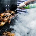 person holding green bottle and grilled meat