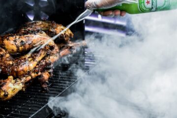 person holding green bottle and grilled meat