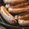 a group of sausages cooking in a frying pan